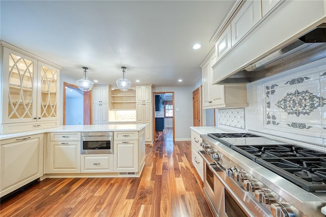 kitchen featuring pendant lighting, premium range hood, light hardwood / wood-style flooring, stainless steel range, and tasteful backsplash