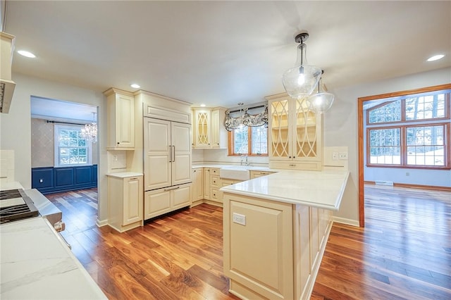 kitchen with light stone countertops, tasteful backsplash, kitchen peninsula, pendant lighting, and hardwood / wood-style flooring