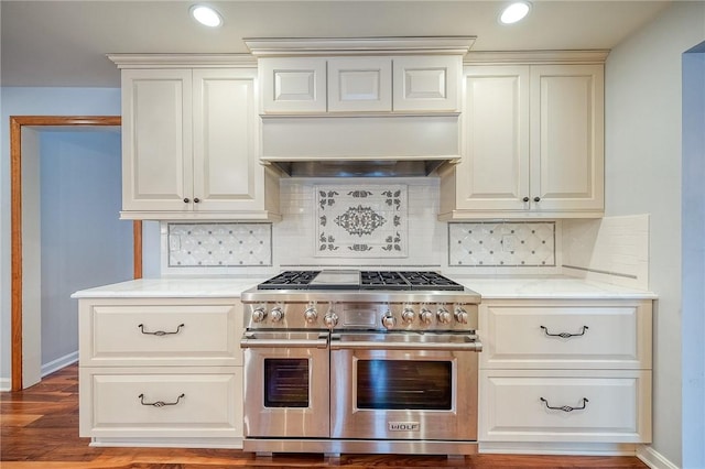 kitchen with light stone counters, range with two ovens, wood-type flooring, and backsplash