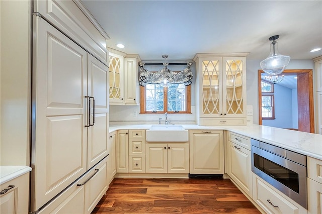 kitchen with dark wood-type flooring, sink, hanging light fixtures, built in appliances, and kitchen peninsula