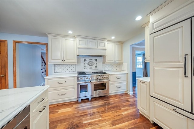 kitchen featuring light stone counters, hardwood / wood-style floors, double oven range, decorative backsplash, and white cabinets