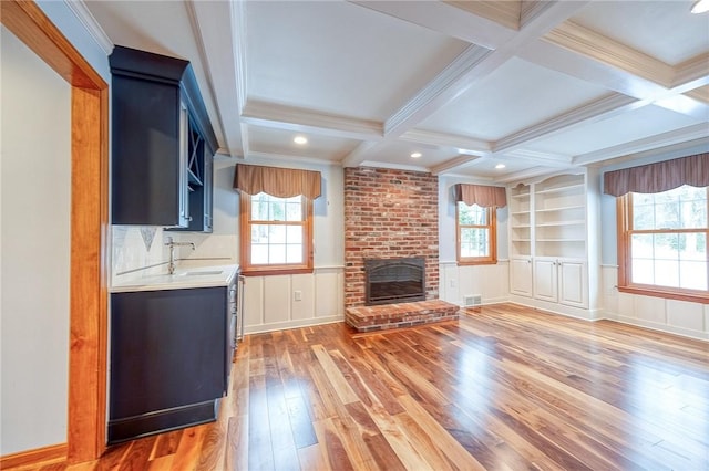 unfurnished living room with a brick fireplace, coffered ceiling, sink, beam ceiling, and hardwood / wood-style floors