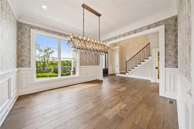 unfurnished dining area with hardwood / wood-style floors, an inviting chandelier, and ornamental molding