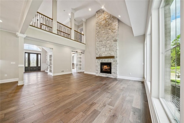 unfurnished living room featuring french doors, a barn door, a towering ceiling, a fireplace, and hardwood / wood-style flooring