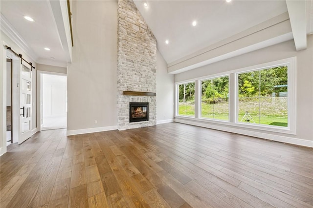 unfurnished living room with wood-type flooring, a barn door, high vaulted ceiling, and a stone fireplace