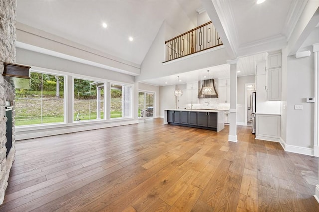 unfurnished living room with decorative columns, high vaulted ceiling, and light hardwood / wood-style flooring