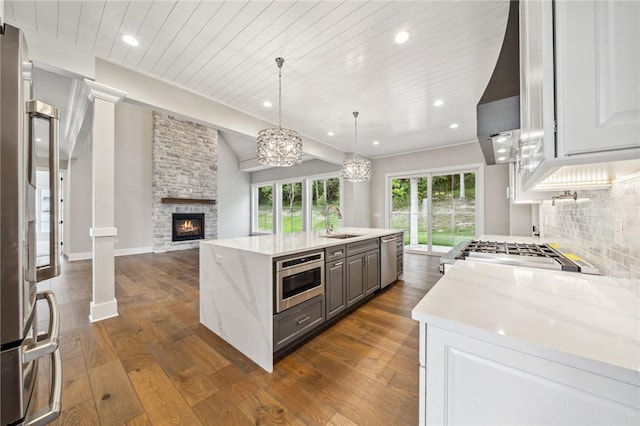 kitchen with appliances with stainless steel finishes, tasteful backsplash, light stone counters, white cabinets, and hanging light fixtures