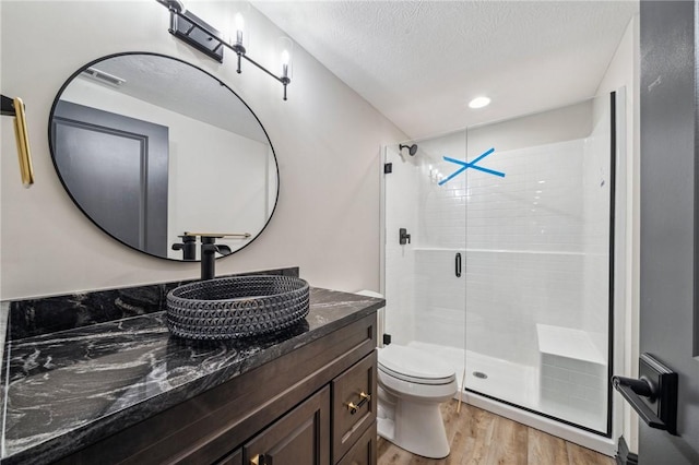 bathroom with vanity, wood-type flooring, toilet, a textured ceiling, and a shower with shower door