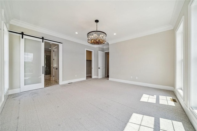 carpeted spare room featuring a barn door, ornamental molding, and a notable chandelier