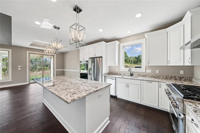 kitchen with sink, appliances with stainless steel finishes, decorative light fixtures, a kitchen island, and white cabinetry