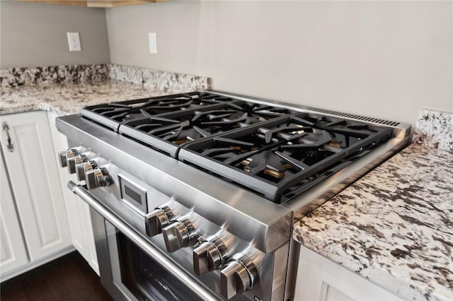 interior details with white cabinets, light stone countertops, and stainless steel stove