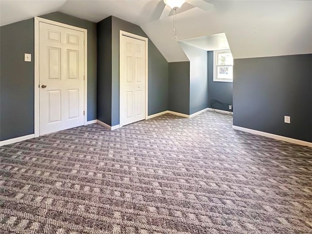 additional living space with dark colored carpet, ceiling fan, and vaulted ceiling