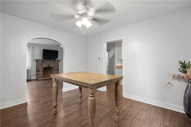 dining room featuring ceiling fan, dark hardwood / wood-style floors, a stone fireplace, and radiator