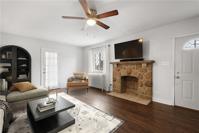 living room featuring a stone fireplace, ceiling fan, radiator heating unit, and wood-type flooring