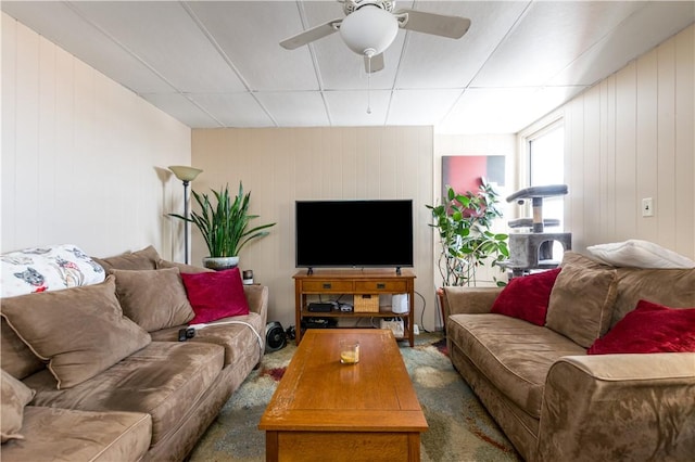 living room featuring a paneled ceiling, wood walls, ceiling fan, and dark colored carpet