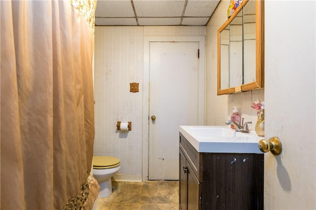 bathroom featuring vanity, a paneled ceiling, toilet, and tile walls