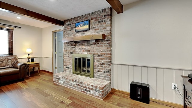 living room featuring a textured ceiling, beam ceiling, light hardwood / wood-style flooring, and a brick fireplace