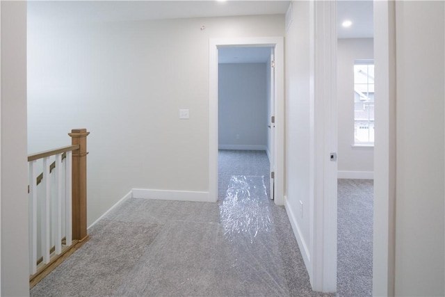 hall featuring carpet floors, baseboards, and an upstairs landing