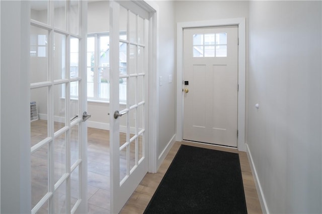 doorway featuring french doors, light wood-style flooring, and baseboards