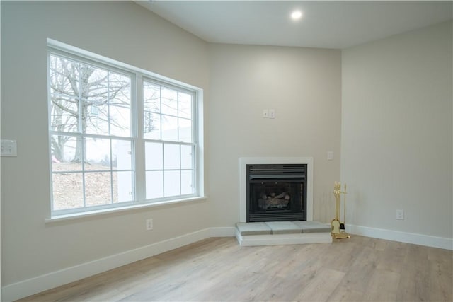 unfurnished living room with baseboards, a fireplace with raised hearth, wood finished floors, and recessed lighting