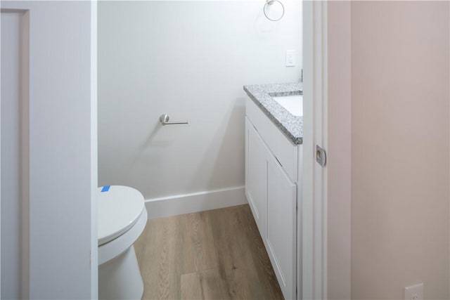 bathroom with toilet, wood finished floors, vanity, and baseboards