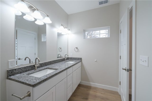 bathroom with double vanity, wood finished floors, a sink, and visible vents