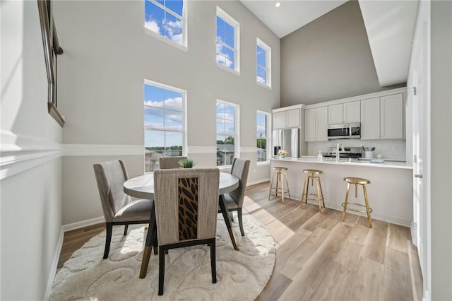 dining space featuring a towering ceiling and light hardwood / wood-style floors