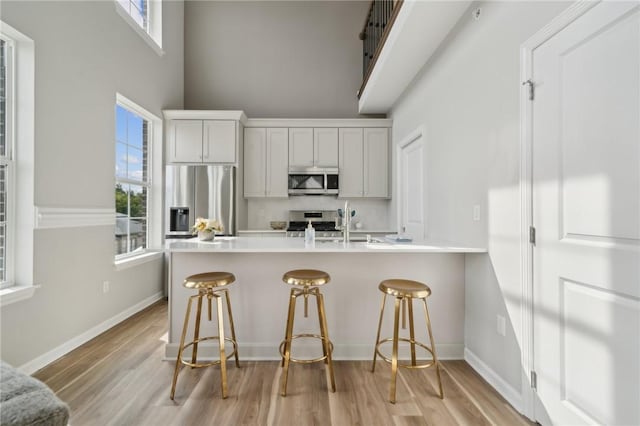 kitchen with white cabinetry, a high ceiling, a breakfast bar, appliances with stainless steel finishes, and light wood-type flooring