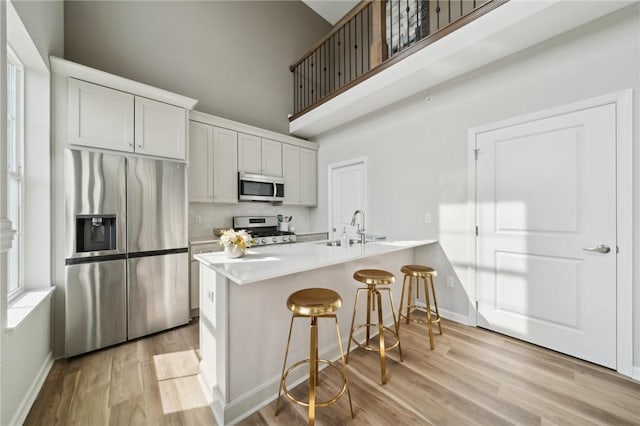 kitchen featuring kitchen peninsula, a kitchen bar, stainless steel appliances, sink, and light hardwood / wood-style flooring