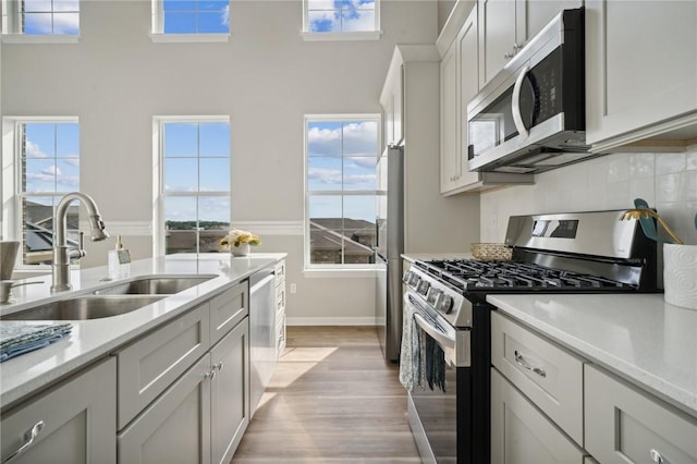 kitchen featuring sink, light wood-type flooring, a high ceiling, and appliances with stainless steel finishes