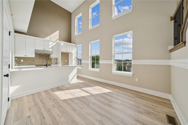 kitchen featuring a high ceiling, sink, light wood-type flooring, tasteful backsplash, and white cabinetry