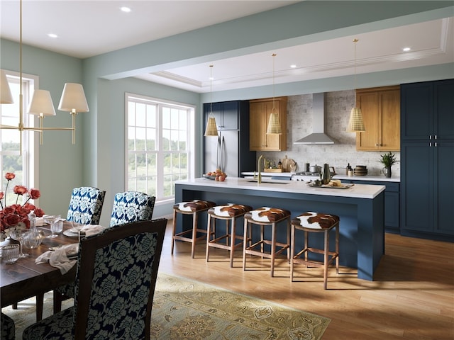 kitchen featuring pendant lighting, backsplash, a kitchen breakfast bar, wall chimney range hood, and stainless steel refrigerator