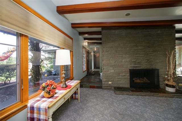 carpeted living room with beamed ceiling and a stone fireplace