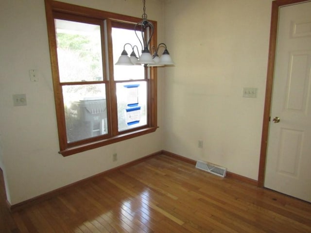 unfurnished dining area featuring a chandelier and wood-type flooring