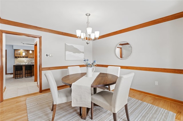 dining space featuring ornamental molding, light wood-type flooring, and a notable chandelier