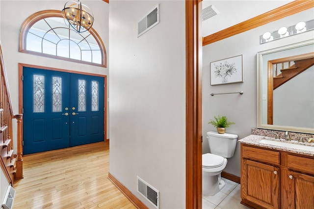 foyer entrance with a high ceiling, crown molding, sink, light hardwood / wood-style floors, and a chandelier