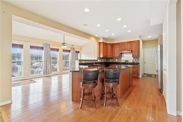 kitchen featuring ceiling fan, a kitchen breakfast bar, light hardwood / wood-style flooring, kitchen peninsula, and appliances with stainless steel finishes