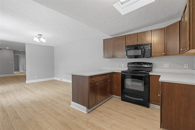 kitchen featuring a skylight, kitchen peninsula, a textured ceiling, black appliances, and light wood-type flooring