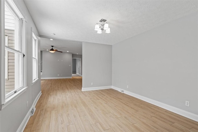 empty room featuring light hardwood / wood-style flooring, ceiling fan with notable chandelier, and a textured ceiling