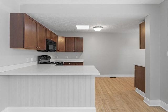 kitchen featuring kitchen peninsula, a textured ceiling, light hardwood / wood-style floors, and black appliances