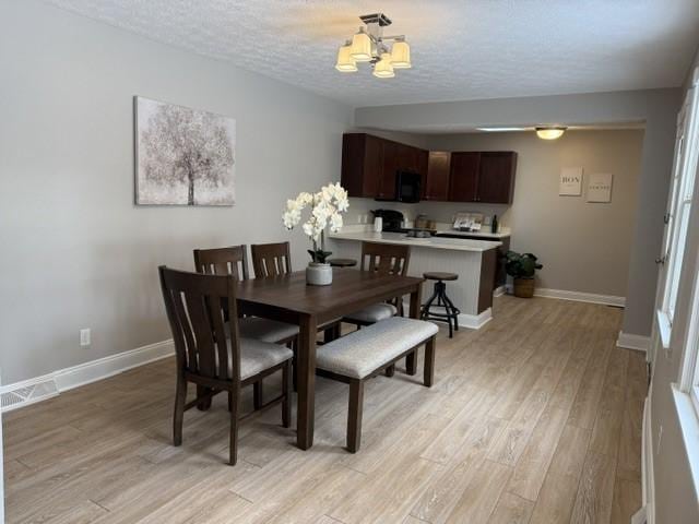 dining area featuring a textured ceiling, light hardwood / wood-style floors, and a notable chandelier