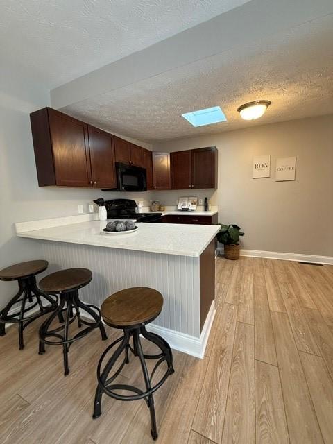 kitchen with black appliances, a kitchen breakfast bar, kitchen peninsula, and a skylight