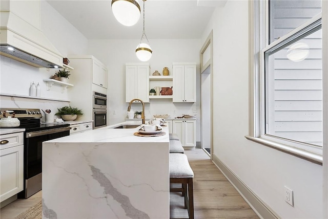 kitchen with sink, light stone counters, a kitchen island with sink, white cabinets, and appliances with stainless steel finishes