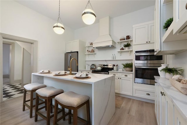 kitchen featuring a center island with sink, custom range hood, a kitchen bar, white cabinetry, and stainless steel appliances