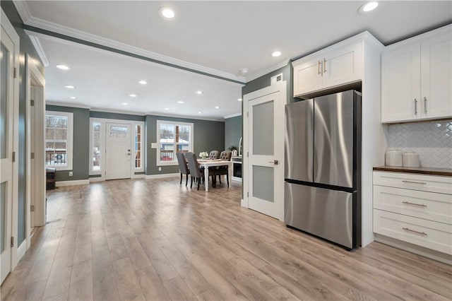 kitchen featuring stainless steel fridge, light wood-type flooring, tasteful backsplash, ornamental molding, and white cabinetry