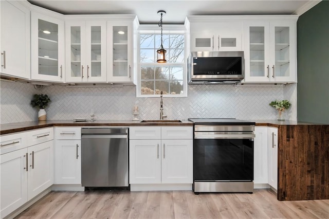 kitchen featuring appliances with stainless steel finishes, sink, light hardwood / wood-style floors, white cabinetry, and hanging light fixtures