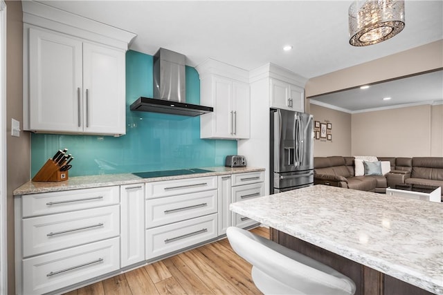 kitchen featuring wall chimney range hood, stainless steel fridge, crown molding, black electric cooktop, and white cabinets