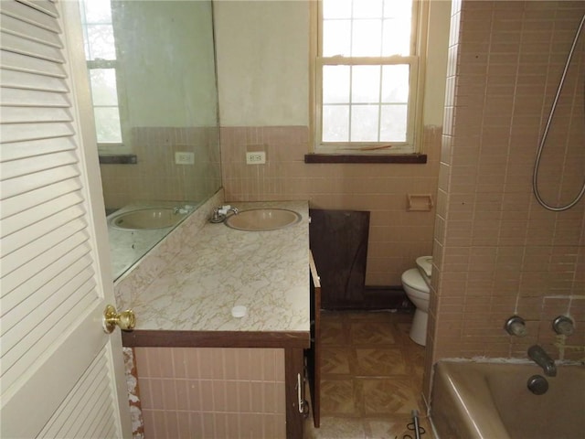 full bathroom with tiled shower / bath, vanity, toilet, and tile walls