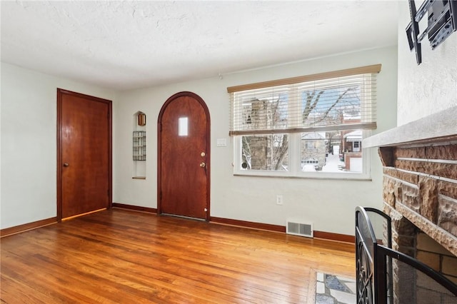 entrance foyer with hardwood / wood-style flooring, a stone fireplace, and a textured ceiling