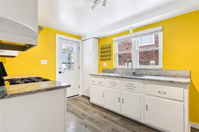 kitchen featuring track lighting, sink, light hardwood / wood-style flooring, white cabinetry, and range with gas stovetop